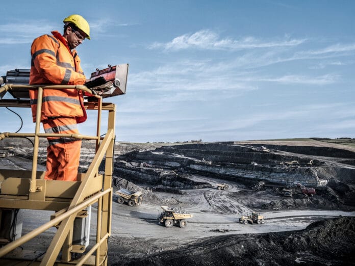 Ecologist using digital tablet surveying surface coal mine site from platform, elevated view